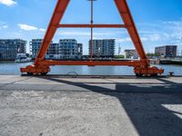 a man is sitting under the big orange structure at a boat dock on a lake