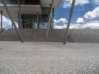 a person on a bike walking through a stone building entrance, in front of an enormous glass wall and stairs