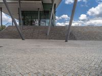 a person on a bike walking through a stone building entrance, in front of an enormous glass wall and stairs