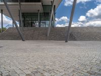 a person on a bike walking through a stone building entrance, in front of an enormous glass wall and stairs