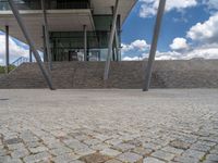 a person on a bike walking through a stone building entrance, in front of an enormous glass wall and stairs