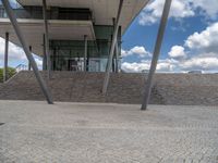 a person on a bike walking through a stone building entrance, in front of an enormous glass wall and stairs