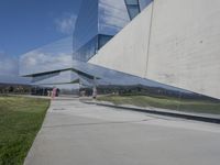 a person walking in front of a modern building, with grass on the side of the walkway