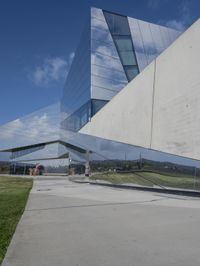 a person walking in front of a modern building, with grass on the side of the walkway