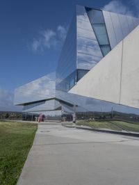 a person walking in front of a modern building, with grass on the side of the walkway