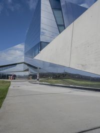 a person walking in front of a modern building, with grass on the side of the walkway