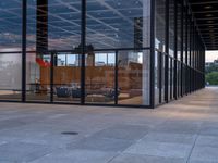 a room with glass walls and an office window, with chairs outside and in the background