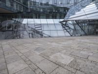 a courtyard that features a glass building with many large windows and a reflection on the wall