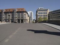 an intersection with buildings and people walking in the foreground and a person riding a skateboard