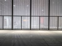 a empty room in a large building with sheer curtained windows overlooking the city on a cloudy day