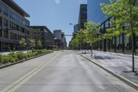 people walk along a deserted street in front of a tall glass building and green trees