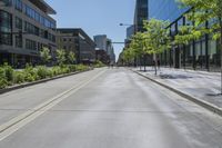 people walk along a deserted street in front of a tall glass building and green trees
