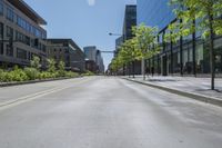 people walk along a deserted street in front of a tall glass building and green trees