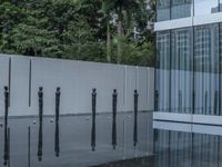 a row of poles sticking out of a glass pool with trees in the background in a city
