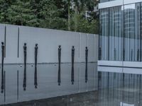 a row of poles sticking out of a glass pool with trees in the background in a city