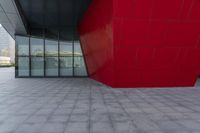 a large red block on the side of a building with a person walking by it