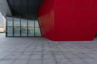 a large red block on the side of a building with a person walking by it