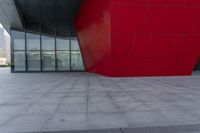 a large red block on the side of a building with a person walking by it