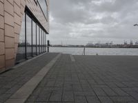 a large long building that has glass windows and a brick sidewalk near it on the side of a river