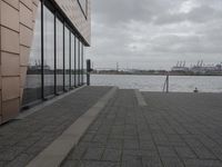 a large long building that has glass windows and a brick sidewalk near it on the side of a river
