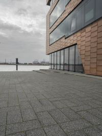 an empty sidewalk next to the water in front of a building with large glass windows