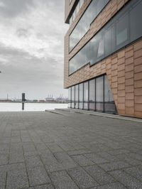 an empty sidewalk next to the water in front of a building with large glass windows