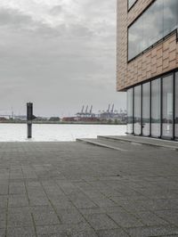 an empty sidewalk next to the water in front of a building with large glass windows