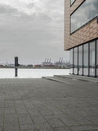 an empty sidewalk next to the water in front of a building with large glass windows