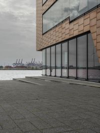 an empty sidewalk next to the water in front of a building with large glass windows