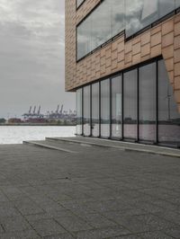 an empty sidewalk next to the water in front of a building with large glass windows