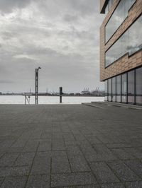 an empty sidewalk next to the water in front of a building with large glass windows