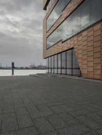 an empty sidewalk next to the water in front of a building with large glass windows