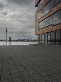 an empty sidewalk next to the water in front of a building with large glass windows