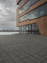 an empty sidewalk next to the water in front of a building with large glass windows