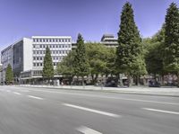 a city street with cars driving by trees and buildings along the road with blue skies