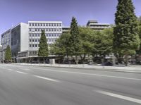 a city street with cars driving by trees and buildings along the road with blue skies