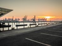 some cars parked near water and a building with some boats in the background at dusk