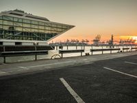 some cars parked near water and a building with some boats in the background at dusk