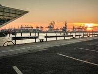 some cars parked near water and a building with some boats in the background at dusk