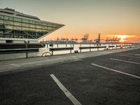 some cars parked near water and a building with some boats in the background at dusk