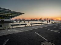 some cars parked near water and a building with some boats in the background at dusk