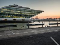 some cars parked near water and a building with some boats in the background at dusk