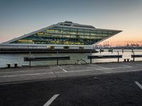 some cars parked near water and a building with some boats in the background at dusk