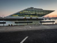 some cars parked near water and a building with some boats in the background at dusk