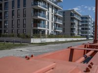 a orange train going down a city street under tall buildings near the sidewalk with a car parked along side it