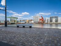 the street has an orange chair on it near the water, with a view of a cranes in the distance