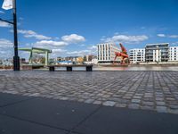 the street has an orange chair on it near the water, with a view of a cranes in the distance