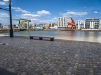 the street has an orange chair on it near the water, with a view of a cranes in the distance