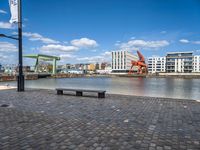 the street has an orange chair on it near the water, with a view of a cranes in the distance