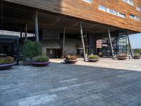 a concrete courtyard with pots of plants and a building that has a wooden roof on it